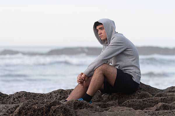 Depressed man sitting on rocks at beach.
